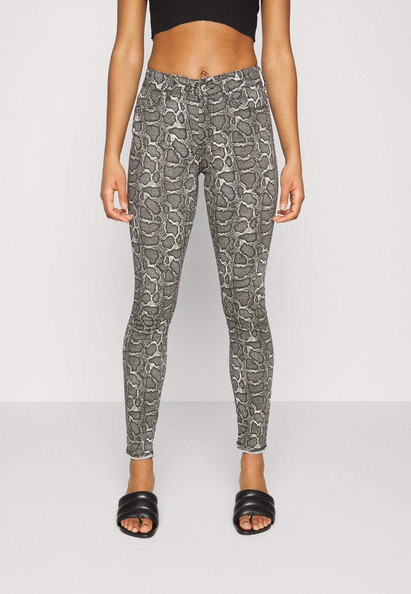 Leggings de estampado de serpiente en blanco y negro con un diseño ajustado, que cuentan con una tela texturizada y una cinturilla elástica. Llevados con sandalias negras tipo slide.