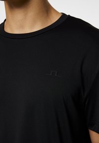 Svart t-shirt med kort ärm och rund halsringning, med en diskret tonality logotyp på bröstet. Slät, lättviktsmaterial med en figursydd design.