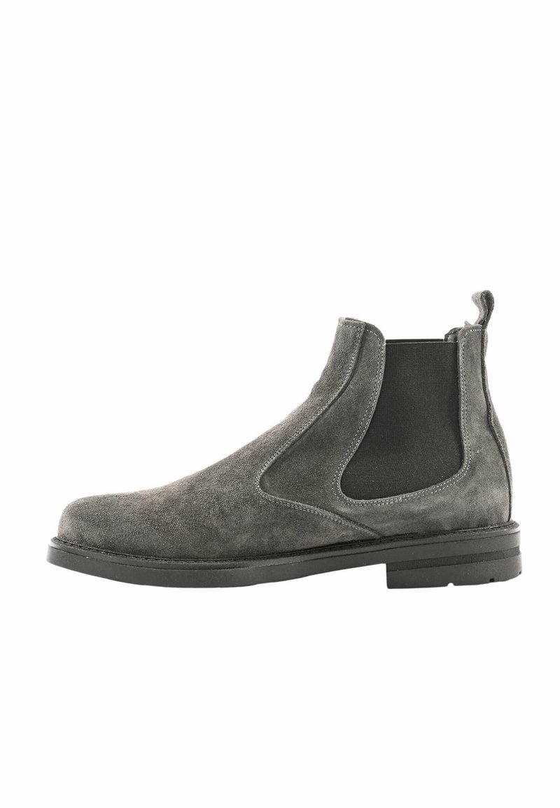 Stivaletto Chelsea in suede grigio con pannelli laterali elastici, punta rotonda, linguetta e suola nera piatta. Superficie testurizzata con dettagli cuciti.