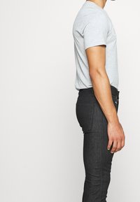 Camiseta gris de algodón con cuello redondo, combinada con jeans de denim negros de corte ajustado y con un sutil cosido en el bolsillo trasero.