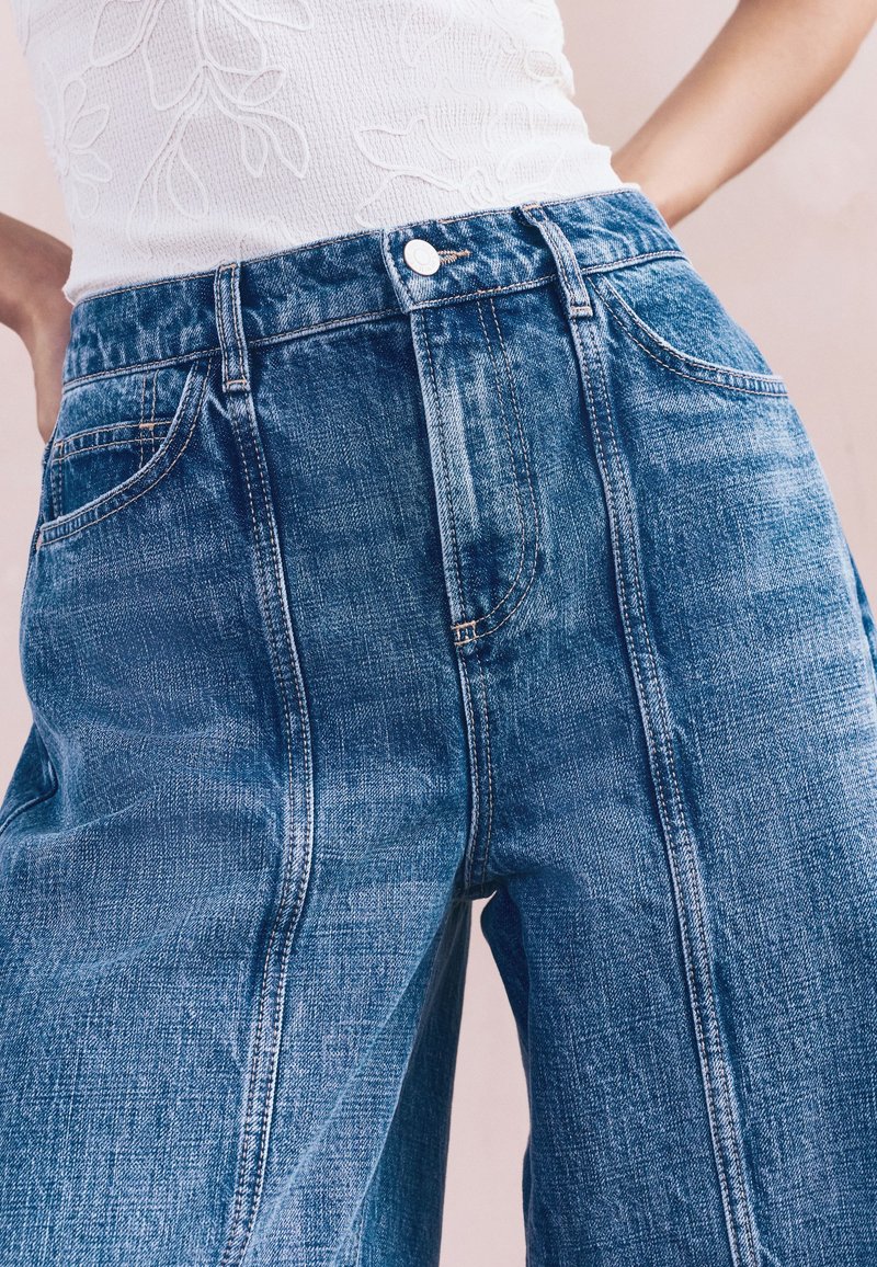 Blaue weite Denim-Jeans mit hoher Taille, auffälligen Nähten, Fronttaschen und einem Verschluss mit Metallknopf.