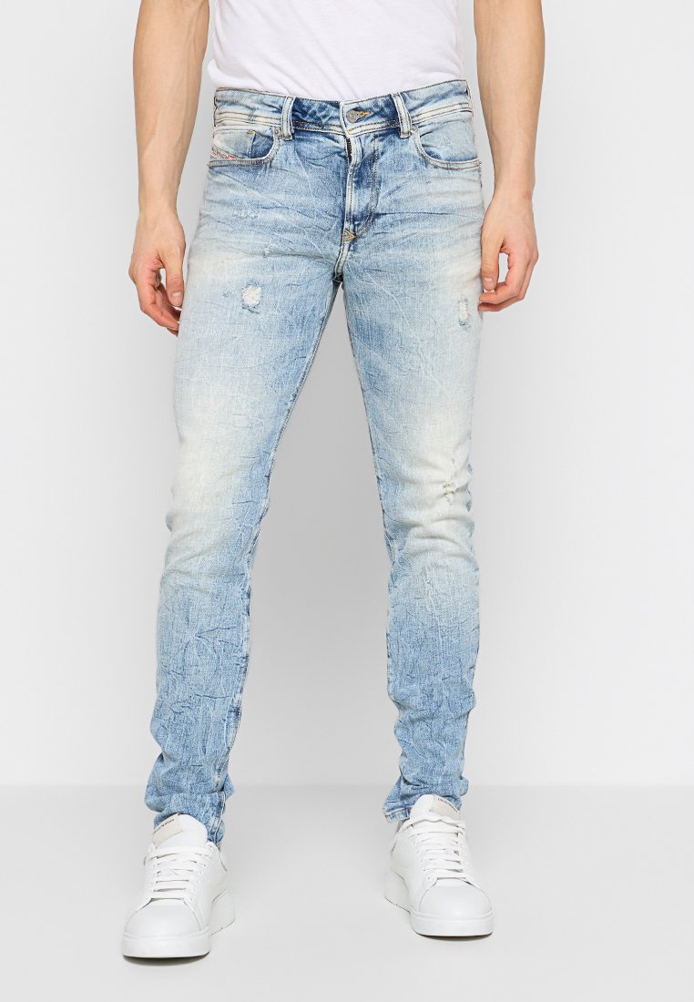 Jeans in denim blu chiaro con vestibilità slim, dettagli strappati e texture sbiadita. Abbinati a sneakers bianche per un look casual.