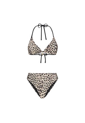 Žena s kučeravými vlasmi v bikinkach so vzorom leoparda stojaca bosá na jednoliatom svetlom pozadí, mierne otočená do boku.