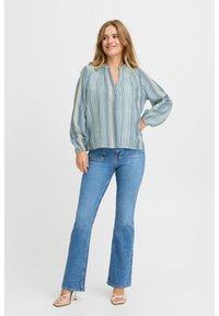 Blusa azzurra con righe verticali, scollatura a V e maniche lunghe. Abbinata a jeans blu aderenti e tacchi a strappo.