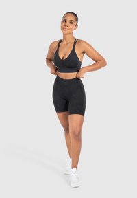 Conjunto atlético negro que incluye un sujetador deportivo con tirantes ajustables y pantalones cortos de talle alto a juego, fabricados en un tejido suave y elástico.