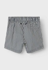 Niebiesko-białe, w paski szorty kąpielowe z elastycznym paskiem w talii, dwoma guzikami i krótkim krojem. Materiał ma gładką, lekką fakturę.