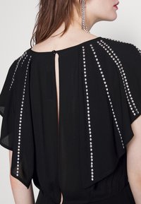 Black dress with flutter sleeves, featuring silver studs arranged in vertical lines, and a keyhole back with a button closure.