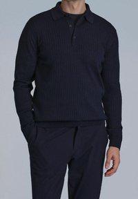 Polo à manches longues bleu marine en texture côtelée avec un col à revers et une patte de boutonnage à trois boutons ; style ajusté, associé à un pantalon bleu marine assorti.