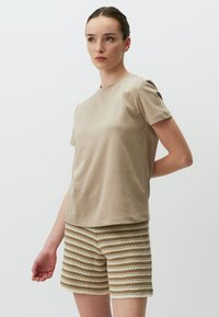Beige Baumwoll-T-Shirt mit kurzen Ärmeln, kombiniert mit strukturierten Shorts, die abwechselnd cremefarbene und hellbraune Streifen aufweisen.
