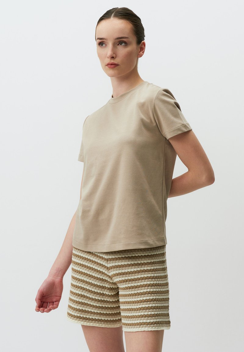Beige Baumwoll-T-Shirt mit kurzen Ärmeln, kombiniert mit strukturierten Shorts, die abwechselnd cremefarbene und hellbraune Streifen aufweisen.