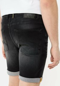 Schwarze Denim-Shorts mit einem ausgewaschenen Finish, mit umgeschlagenen Säumen, Gesäßtaschen und einem schwarzen Logo-Patch am Bund.