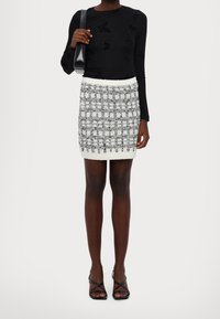 Haut noir à manches longues avec motif papillon, associé à une mini-jupe à carreaux texturée blanche et grise, et des sandales à talons hauts noires à lanières.