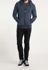 Granatowa bluza z kapturem na zamek błyskawiczny z troczkami, przednimi kieszeniami i naszywką z logo, w połączeniu z czarnymi, dopasowanymi dżinsami i ciemnymi trampkami.