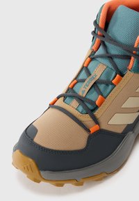 Lightweight hiking shoe in beige, dark gray, and teal. Features textured upper, orange accents, and rugged rubber sole with prominent tread.