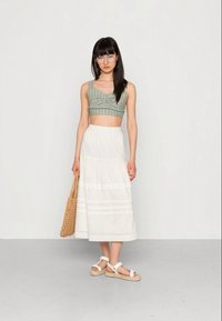Top crop listrado verde claro, saia midi branca em camadas, bolsa de vime e sandálias brancas com tiras. O conjunto apresenta um design descontraído.