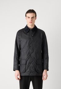 Veste en coton ciré noir avec un col en velours, des boutons sur le devant et deux poches plaquées. Présente une texture lisse et une coupe ajustée.