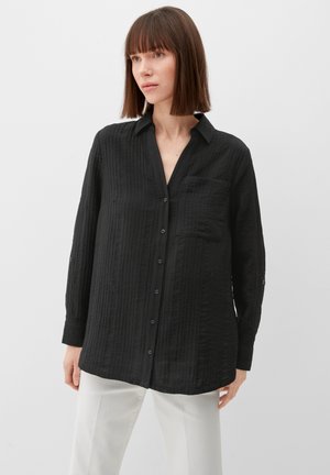 Chemise noire à boutons, en tissu texturé, avec un col, des manches longues et une poche unique sur la poitrine gauche. Motif à rayures verticales.