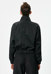 Zwarte nylon jas met een hoge kraag, elastische taille en lange mouwen. Gladde textuur, minimaal ontwerp en geen opvallende patronen of hardware.