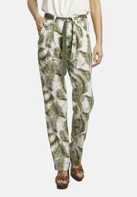 Pantalones de tela blanca con un patrón de hojas de palma verdes, con cinturilla ajustable, dos bolsillos laterales y un ajuste cómodo. Combinados con sandalias de tacón marrones.
