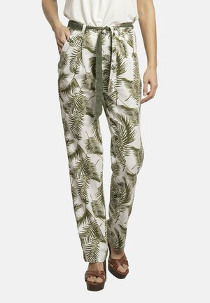 Pantalones de tela blanca con un patrón de hojas de palma verdes, con cinturilla ajustable, dos bolsillos laterales y un ajuste cómodo. Combinados con sandalias de tacón marrones.