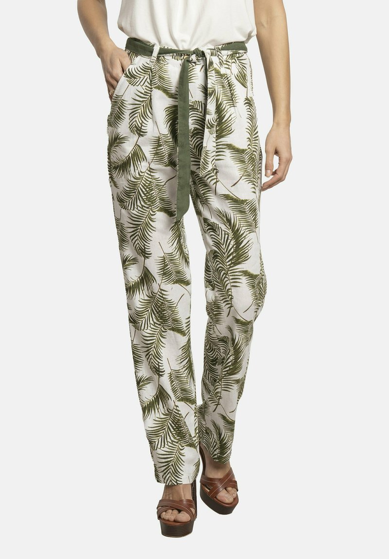 Pantalones de tela blanca con un patrón de hojas de palma verdes, con cinturilla ajustable, dos bolsillos laterales y un ajuste cómodo. Combinados con sandalias de tacón marrones.