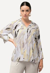 Blusa leggera bianca con motivi astratti gialli, grigi e neri. Presenta un collo a V e maniche a tre quarti, dalla texture morbida.