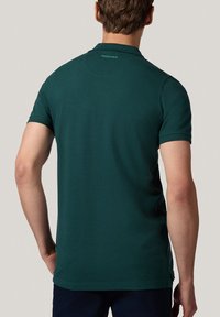 Ciemnozielona koszulka polo, krótki rękaw, klasyczny kołnierzyk, gładka faktura, dyskretne logo "PROCHNIK" przy szyi oraz dopasowany krój.