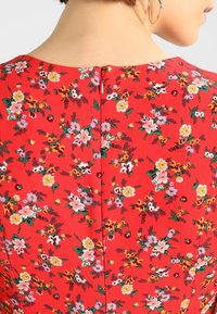 Rotes Kleid mit floralem Muster und verschiedenen farbigen Blumen, strukturiertem Stoff und einem Reißverschluss auf der Rückseite.