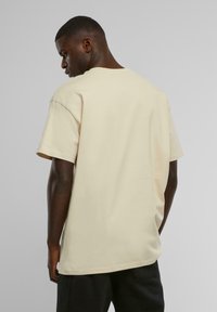 Overdimensjonert beige bomull T-skjorte med korte ermer, rund hals, og en jevn tekstur, vist fra baksiden.