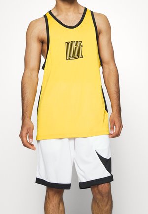 Mężczyzna w żółtej bezrękawnikowej koszulce sportowej Nike z czarnym wykończeniem i białych spodenkach z czarnymi akcentami na jednolitym tle.