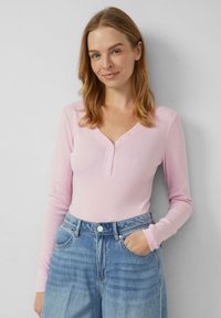 Różowy prążkowany top z długim rękawem, dekoltem w serek i trzema guzikami. W zestawie z jasnoniebieskimi dżinsami z wysokim stanem, posiadającymi przednie kieszenie.