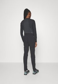 Black athletic long-sleeve top and matching pants. Top features a fitted cut, while pants have zippered pockets. Footwear is black with teal accents.