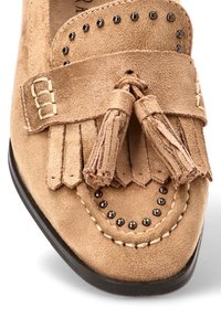 Mocasines de ante en tono claro con borlas y flecos, adornados con tachuelas negras y costuras en contraste a lo largo de la suela.