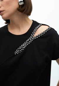 Black t-shirt featuring a decorative embellishment of rhinestones on the shoulder, with a comfortable fit and soft texture.