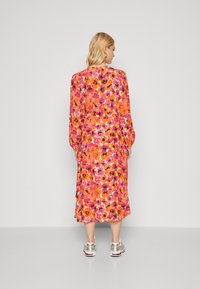 Blommig klänning i medellängd med ett livfullt mönster av rosa, orange och svart; långa ärmar och en flödande siluett. Matchad med metalliska sneakers.