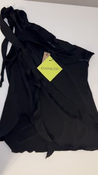 Black sleeveless top with a flowing design; features straps, ruffled layers, and a tag from the brand even&odd in bright green.