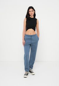 Μαύρο αμάνικο crop top με στριφτό εμπρός μέρος, συνδυασμένο με ανοιχτό μπλε φόρμα με ελαστική μέση και πλαϊνές τσέπες.