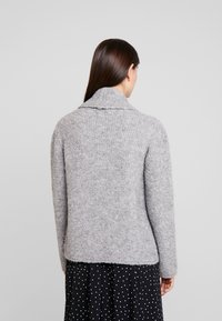 Grå stickad tröja med en bred krage och texturerad yta, figursydd design och ribbad nederkant, i kombination med en prickig kjol.