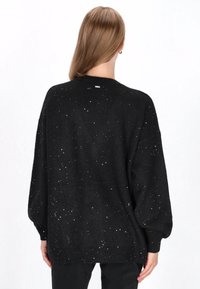 Czarny sweter z dzianiny o luźnym kroju i długich rękawach, z fakturowanym wzorem białych plamek oraz ściągaczem u dołu.