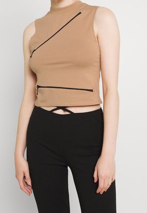 Brown sleeveless crop top made of cotton, featuring two diagonal black zippers and a high neck design, paired with black fitted pants.