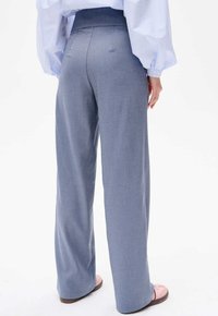 Wijduitlopende broek in lichtblauwe stof met een zachte textuur, voorzien van een hoge taille en discrete achterzakken. Platte schoenen maken de look compleet.