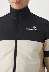 Giacca zip-up nera e crema con colletto alto, caratterizzata da un tessuto texture e il logo di Sergio Tacchini sul petto.