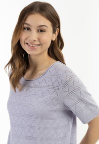 Levandulový pletený top s geometrickým vzorem a otevřenými detaily. Krátké rukávy a zaoblený výstřih dotvářejí design.