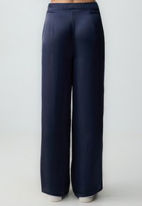 Pantalons larges bleu marine en tissu lisse, avec une taille élastique et deux poches arrière ; présentent un design ajusté et un style minimaliste.