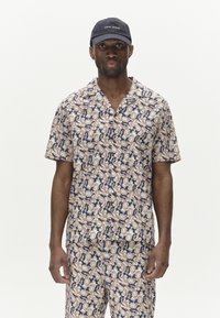 Short-sleeved shirt and matching pants in a cream and navy floral pattern, made of lightweight fabric; paired with a dark blue cap.