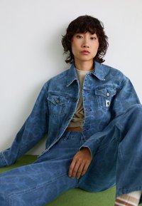 Veste en denim avec un imprimé animal bleu, comportant deux poches avant, une fermeture boutonnée et un pantalon en denim bleu assorti. Texture douce et coupe décontractée.