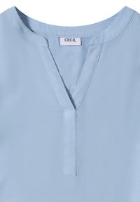 Lyseblå bluse med V-udskæring, korte ærmer og en glat stofstruktur med en central knaplukning og et mærke med teksten "CECIL."