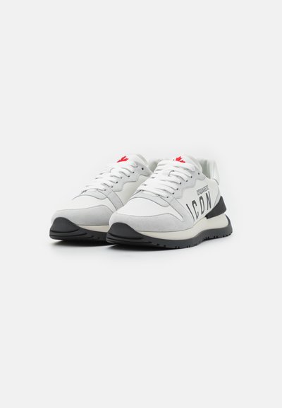Hvite sneakers med grå semsket skinn detaljer, en svart gummisåle og fremtredende "ICON"-merke. Rød logo detalj på tungen.