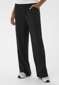 Sorte, brede sweatpants med en glat overflade, der har sidelommer og en afslappet pasform, parret med hvide og grå træningssko.