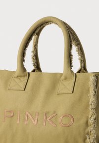 Olivenfarget canvas totebag med slitte håndtak og sideakenter. Har broderte "PINKO" i lys brunt. Kvadratisk søm på stroppene.